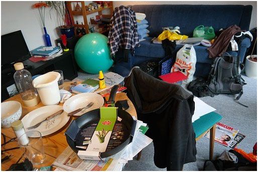 Cluttered living room with scattered household items, including a balance ball, bags, and magazines.