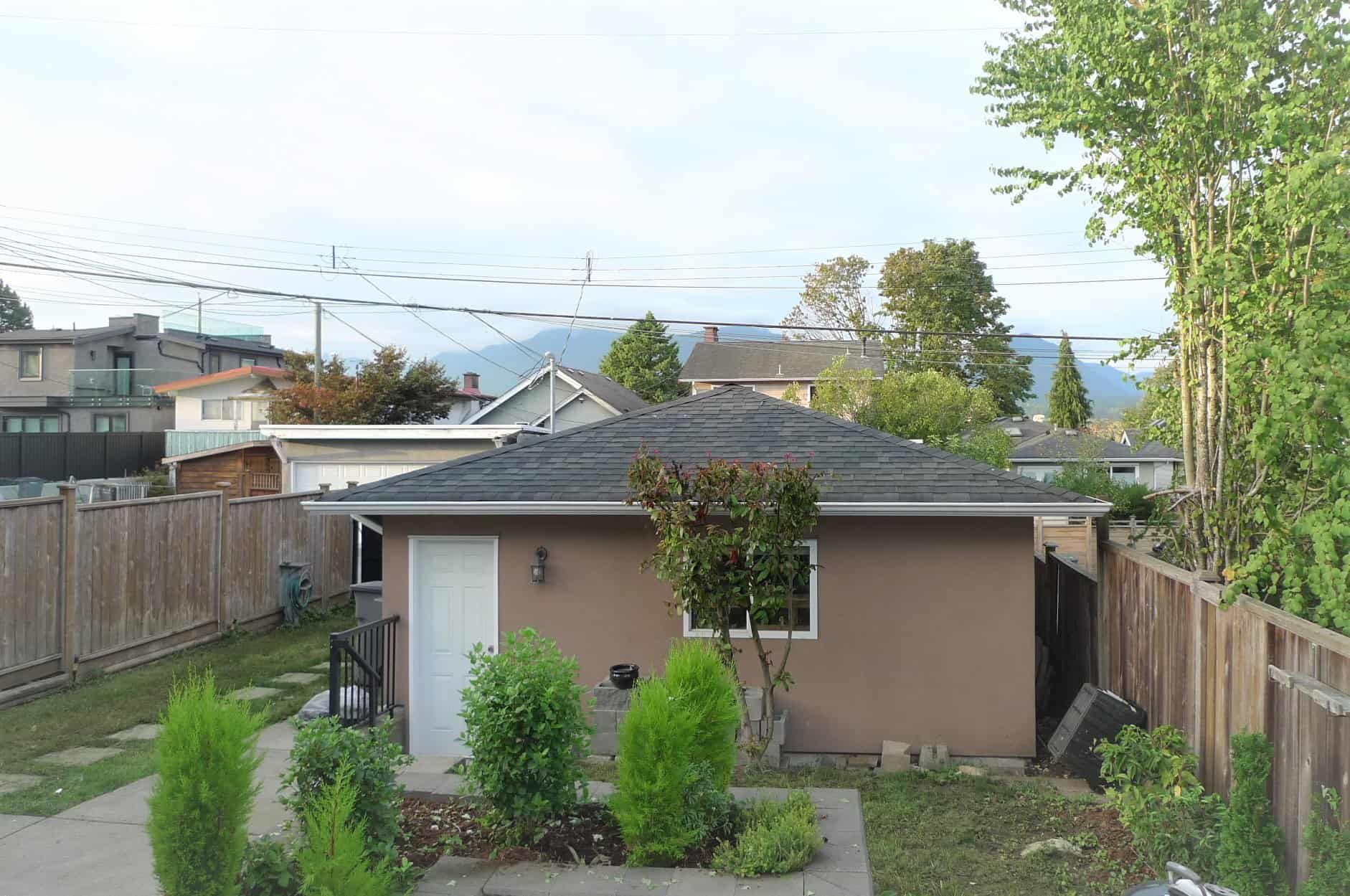 Cozy backyard with small garden and mature trees, enclosed by wooden fencing, in a residential neighborhood with surrounding houses and greenery.