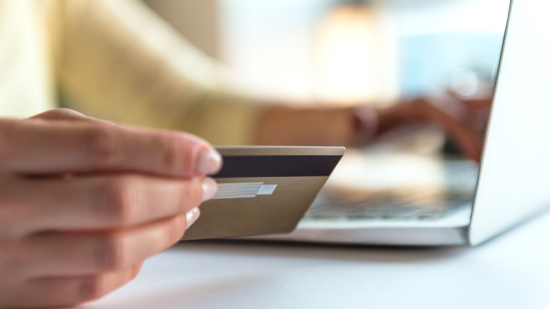 Hand holding a credit card beside a laptop, paying online
