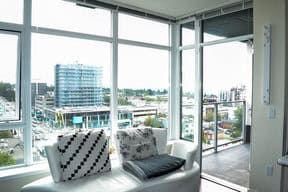 View of modern cityscape from a bright apartment with large windows, featuring comfortable seating, ideal for BC real estate listings and urban living in Vancouver.
