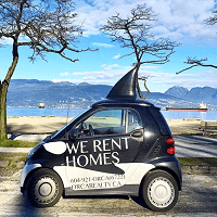 We rent homes,orca realty inc., compact black car with sailboat on roof parked near lake with trees and mountains in background, showcasing real estate rental services in British Columbia, ORCA Realty Inc. specializes in property rentals and real estate solutions in BC, featuring a distinctive rental vehicle with sailboat signage.
