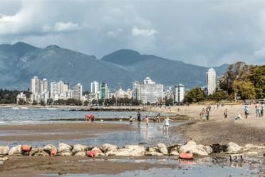 Beach view of a coastal city with modern high-rise buildings and mountain backdrop in Vancouver, BC, Canada, showcasing real estate and waterfront living opportunities.