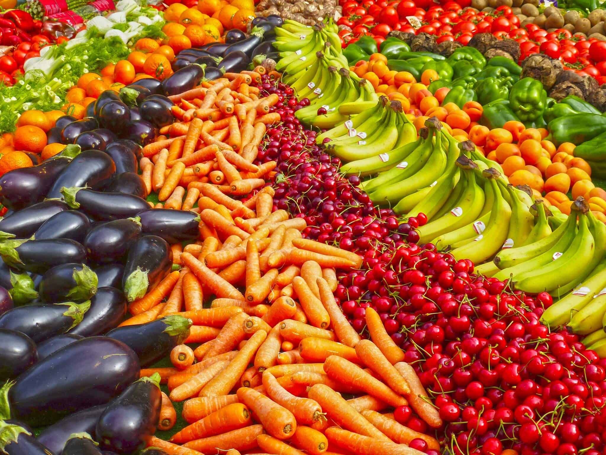 Fresh local produce at a farmer's market, including eggplants, carrots, cherries, bananas, bell peppers, and tomatoes, showcasing vibrant colours and healthy vegetables.