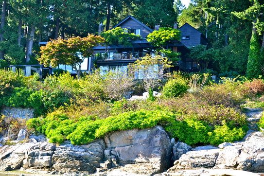 Beautiful waterfront home surrounded by lush greenery and rocky shoreline, showcasing prime real estate for sale in BC. Perfect for those seeking exclusive oceanfront properties.