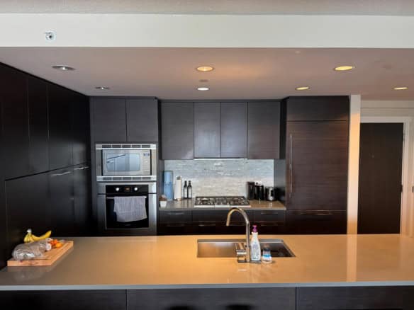 Modern kitchen with dark wood cabinetry, built-in oven and microwave, beige countertop, and stainless steel appliances including a kettle and coffee maker, ideal for Vancouver Island homebuyers.