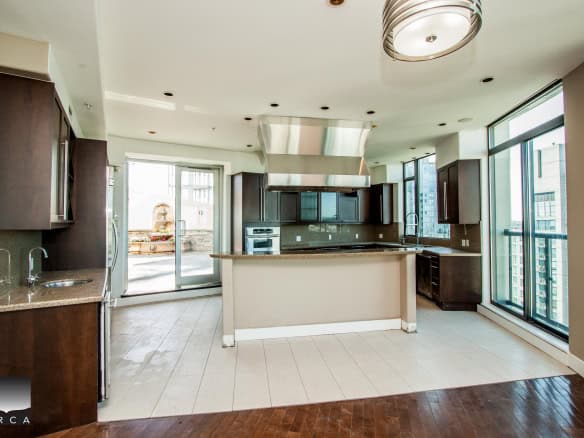 Spacious modern kitchen with dark wood cabinets, granite countertops, stainless steel appliances, and large windows offering city views, ideal for upscale downtown Vancouver condos.