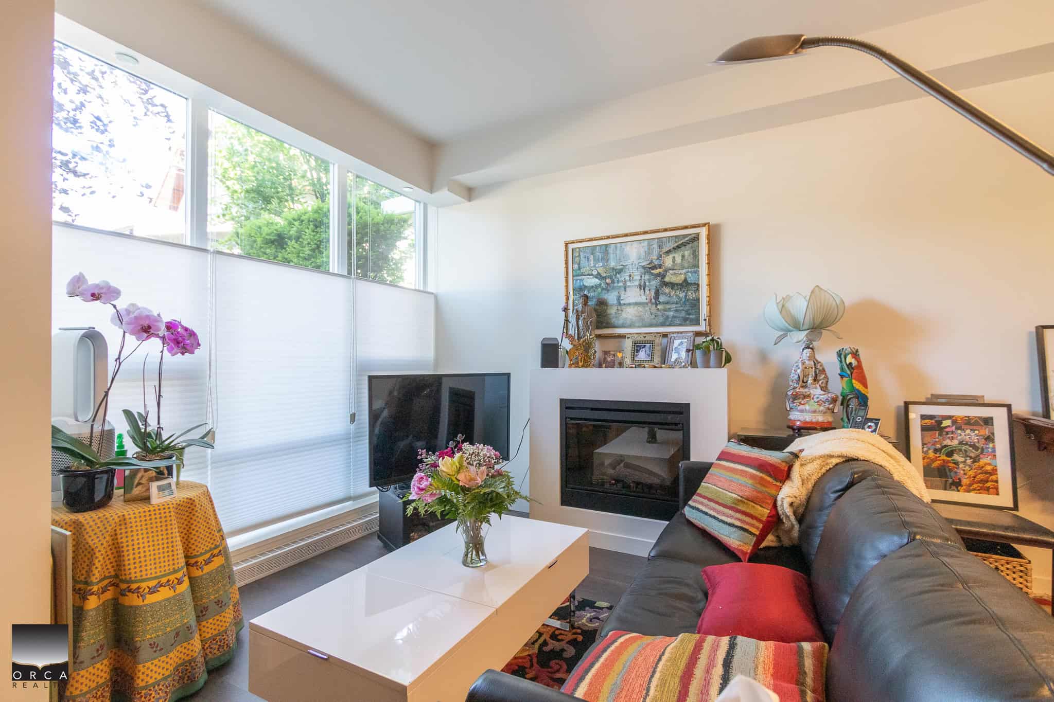 Cozy living room with modern fireplace, large window with natural light, colorful sofa, and stylish decor featuring artwork and sculptures, perfect for Vancouver Island real estate.