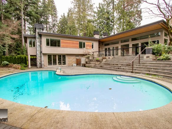 Stylish modern house with backyard pool surrounded by lush forest, featuring large glass windows, outdoor seating area, and multi-level deck, ideal for luxury living and outdoor entertaining in Vancouver BC.