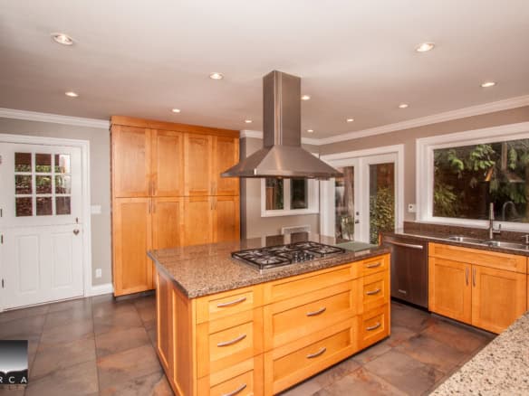 Stunning modern kitchen with wooden cabinetry, granite countertops, stainless steel appliances, and large windows offering natural light, ideal for Vancouver Island real estate.