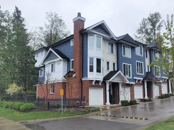 Modern multi-story townhouses with blue and white exterior, brick accents, and landscaped front yards, available through Orca Realty Inc. in a scenic, green neighbourhood in Canada.