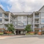 Modern condominium building with multiple balconies and large windows, landscaped entrance, situated in a scenic urban setting, ideal for real estate investments or homeownership in BC.