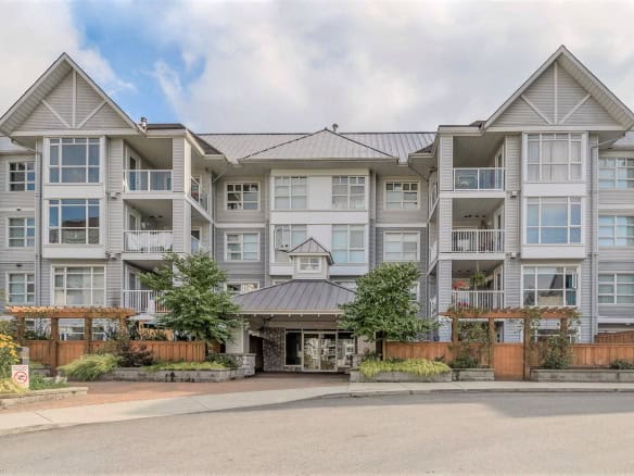 Modern condominium building with multiple balconies and large windows, landscaped entrance, situated in a scenic urban setting, ideal for real estate investments or homeownership in BC.