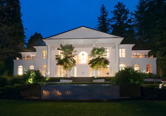 Luxurious waterfront mansion exterior at night, showcasing elegant architecture and lush landscaping for upscale real estate in Vancouver, BC.