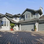 Luxurious multi-story home with stone and wood exterior, spacious driveway, and modern architectural design, available through Orca Realty Inc., located in a desirable neighbourhood in British Columbia.