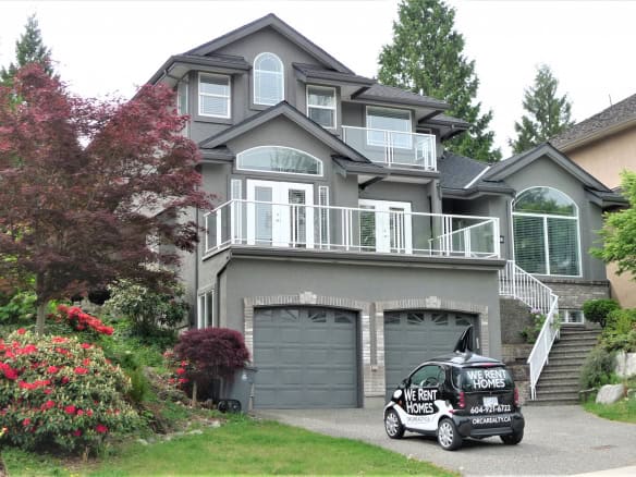 Spacious modern grey house with multiple balconies and large windows, surrounded by lush greenery and colorful landscaping, available for rent through Orca Realty Inc.