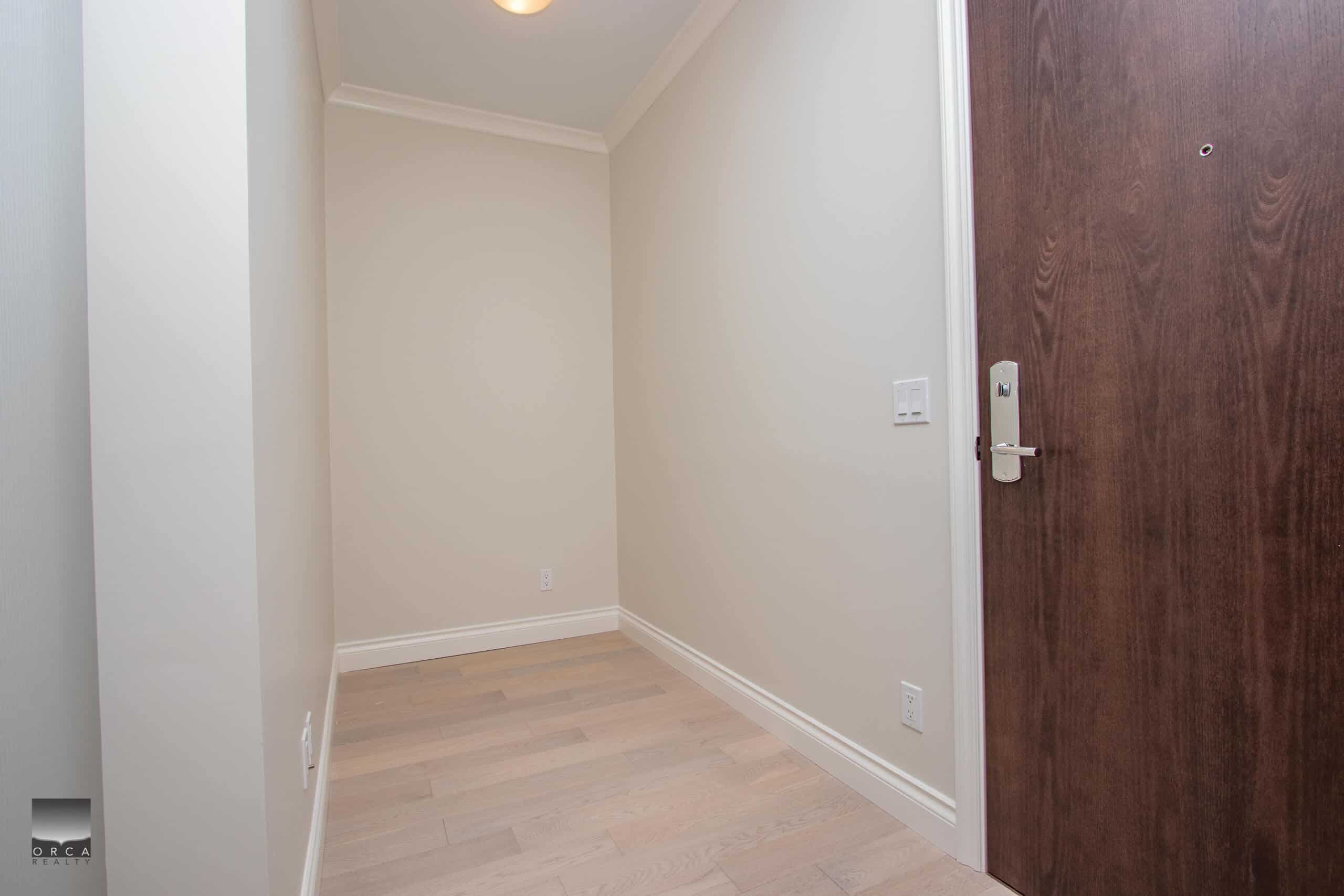 Bright modern interior space with light wood flooring, neutral walls, and a sleek wooden door, showcasing the quality and style of Orca Realty Inc. for Vancouver real estate listings.