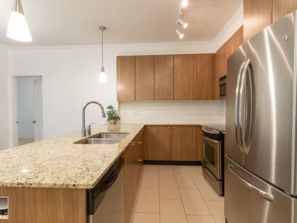 Spacious modern kitchen with granite countertops, stainless steel appliances, and wooden cabinets, ideal for Vancouver real estate buyers seeking contemporary homes.