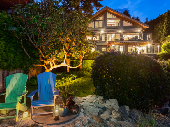 Colorful outdoor chairs on a garden patio overlooking a luxurious modern home illuminated at dusk, showcasing Orca Realty Inc. services in Vancouver and surrounding areas.