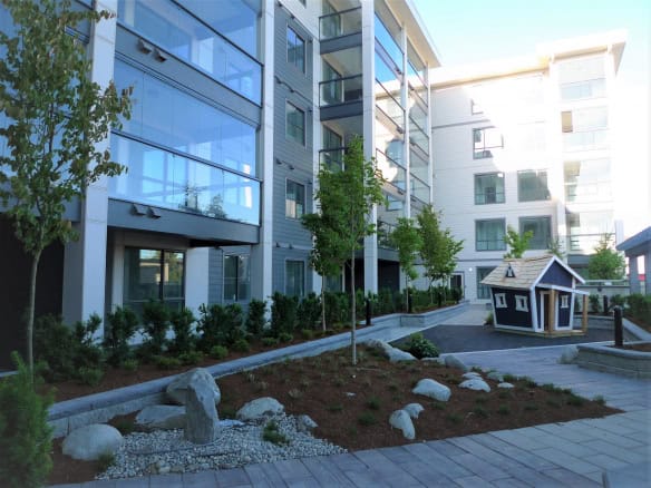Modern apartment complex with landscaped outdoor communal space featuring small trees, rocks, and a playhouse, showcasing contemporary urban living in Vancouver.