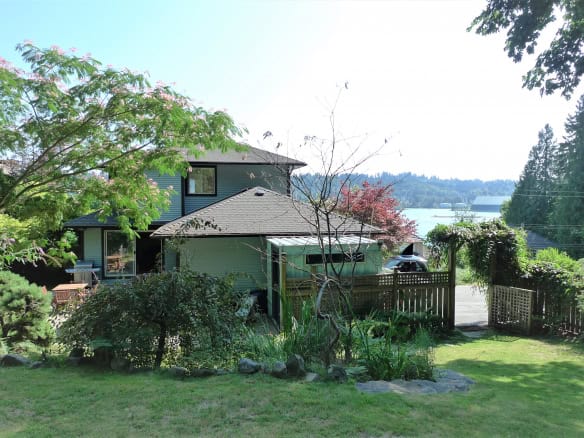 Lush backyard garden with mature trees, vibrant greenery, and scenic water views, showcasing a peaceful outdoor space in a Vancouver Island residential property listed by Orca Realty Inc.