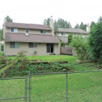 Spacious backyard of a multi-story family home with a green lawn, garden beds, and a tall evergreen tree, ideal for outdoor living and gardening.