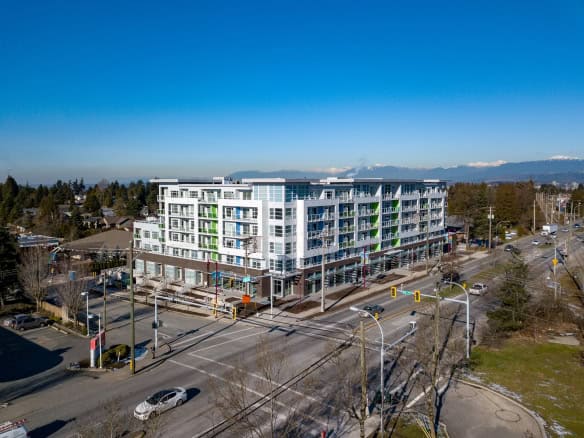 Modern multi-story residential building with retail spaces at street level, located in a vibrant urban area with mountain views in the background.