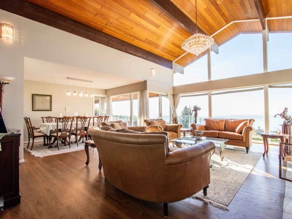 Stunning living room with floor-to-ceiling windows showcasing ocean views, featuring elegant furniture, a wooden vaulted ceiling, and contemporary decor, perfect for luxury real estate in Victoria BC.