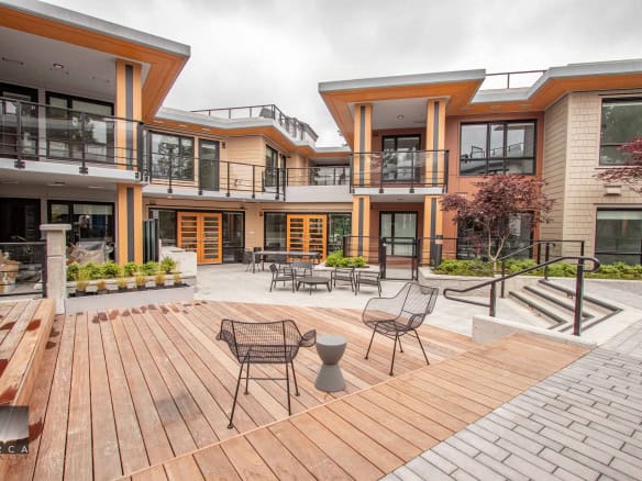 Contemporary modern residential complex with outdoor gathering space, patio furniture, and landscaped greenery, showcasing Orca Realty Inc.'s expertise in Vancouver Island real estate.