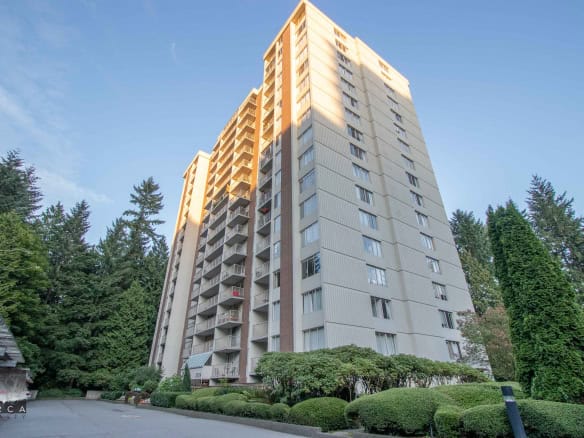 Spacious high-rise apartment building with modern exterior in Vancouver's lush green surroundings, featuring balconies and large windows for city and nature views.