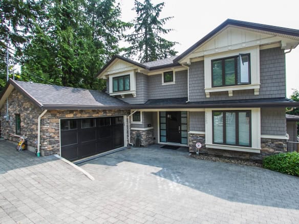 Spacious modern two-storey house with a stone-and-siding exterior, large front driveway, lush greenery, located in a serene neighbourhood. Perfect for families seeking luxury real estate in Vancouver.