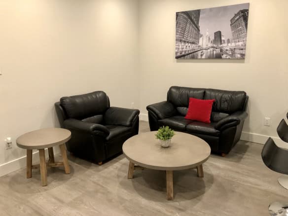 Modern living room with black leather sofas, light wood coffee table, and minimalist decor, including a red cushion and a cityscape artwork, creating a stylish and comfortable space.