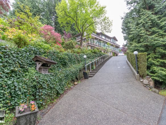 Lush landscaped driveway leading to a beautiful hilltop home, surrounded by vibrant greenery and blooming flowers. Ideal for showcasing luxury property listings in Vancouver.
