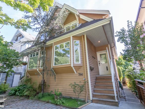 Charming modern house with lush greenery, bay windows, and a cozy front porch, showcasing prime real estate in a vibrant Vancouver neighbourhood, featured by Orca Realty Inc.