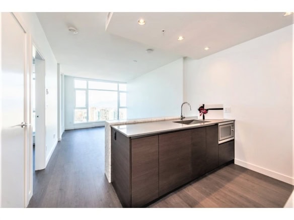 Bright modern kitchen with dark cabinetry, white countertops, stainless steel sink, microwave, and large windows with city views in a contemporary apartment.