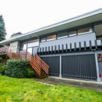 Contemporary modern house with sleek design, large windows, and wooden accents, situated in a lush green landscape in Vancouver, British Columbia. Perfect for luxury real estate buyers.