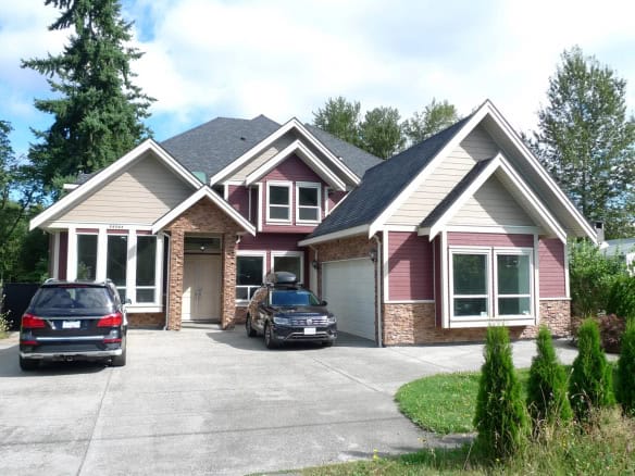 Modern custom-built house with contemporary architecture, featuring a mix of stone, siding, and large windows, located in a lush green neighbourhood in British Columbia, Canada.