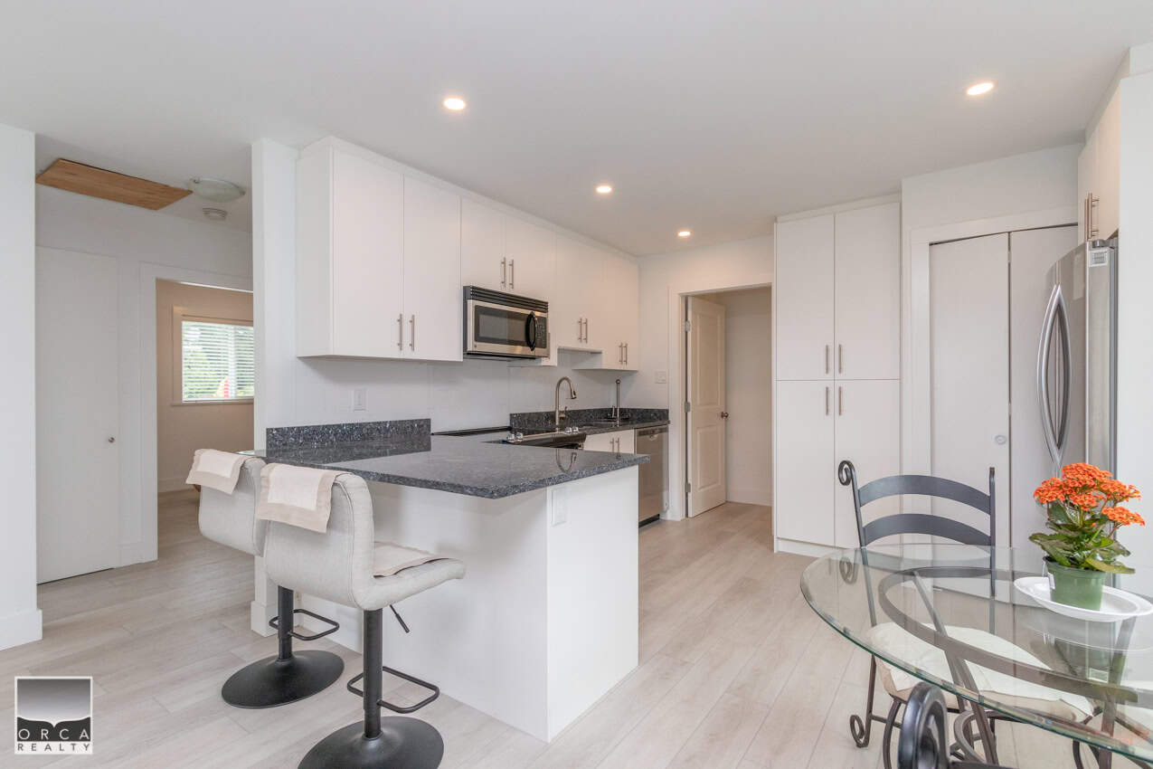 Modern kitchen with white cabinets and granite countertops, stainless steel appliances, and a cozy dining area with a glass table and floral decor, perfect for relaxed living.