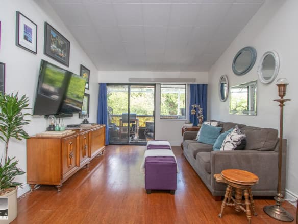 Cozy living room with hardwood floors, modern decor, and large window views, ideal for Vancouver Island real estate, featuring a comfortable sofa, wall-mounted TV, and indoor-outdoor space access.