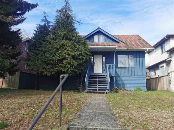 Charming blue house for sale in Vancouver, featuring a welcoming front yard, charming porch, and lush greenery; ideal for families seeking a cozy home in a vibrant neighbourhood.