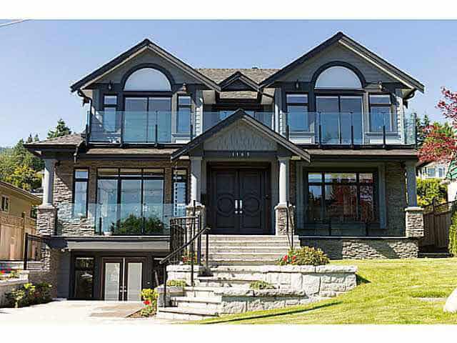 Luxurious modern two-storey house with large glass windows and balcony, situated in a lush green landscape in Vancouver, British Columbia, showcasing upscale real estate opportunity.