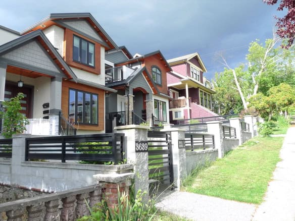 Colorful modern multi-family homes along a sloped street in a vibrant neighbourhood in Vancouver, BC, showcasing contemporary architecture and lush greenery, perfect for real estate investment or family living.
