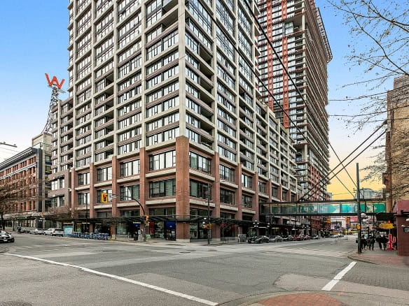 Modern high-rise condo building in Vancouver downtown with retail shops on ground floor, city streets and busy intersection, perfect for real estate investment and urban living.