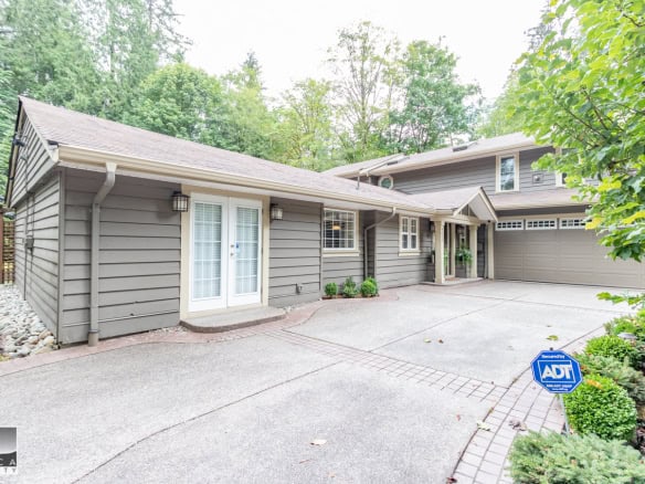 Bright grey modern home exterior with double garage, surrounded by lush greenery and landscaped yard, features in Orca Realty Inc. property listings, ideal for buyers seeking serene suburban homes.