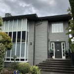Modern grey residential house with black front door, landscaped garden, and large corner windows, showcasing contemporary architecture in British Columbia.