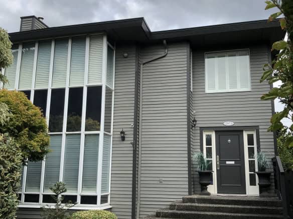 Modern grey residential house with black front door, landscaped garden, and large corner windows, showcasing contemporary architecture in British Columbia.