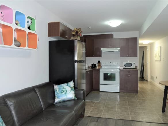 Bright, modern kitchen and living room space in a residential property featuring dark wood cabinets, stainless steel appliances, and a cozy seating area with decorative pillows, ideal for family living.