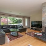 Cozy living room with large window, modern black leather sectional, and stone fireplace, perfect for family gatherings or relaxing at home.