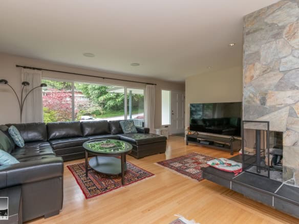 Cozy living room with large window, modern black leather sectional, and stone fireplace, perfect for family gatherings or relaxing at home.