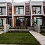 Modern townhouse exterior with contemporary design, wood accents, large windows, and landscaped front yard in a new residential community.