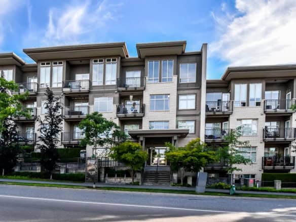 Contemporary multi-story condominium building with large windows and balconies, situated along a tree-lined street with well-maintained landscaping, showcasing modern real estate in Vancouver BC.